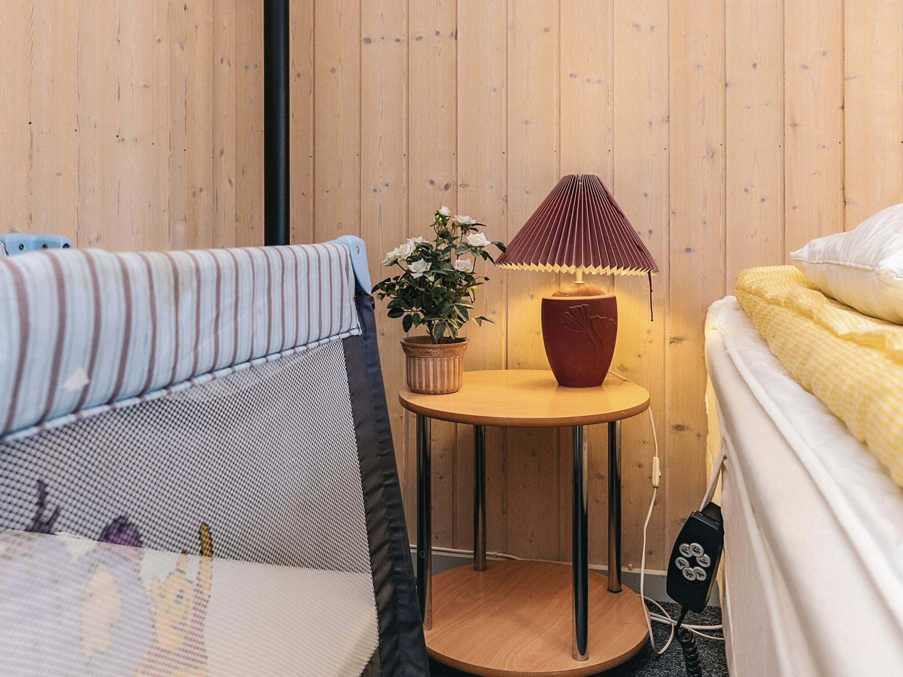 A room with two beds, a small round table with a lamp, and a potted plant.