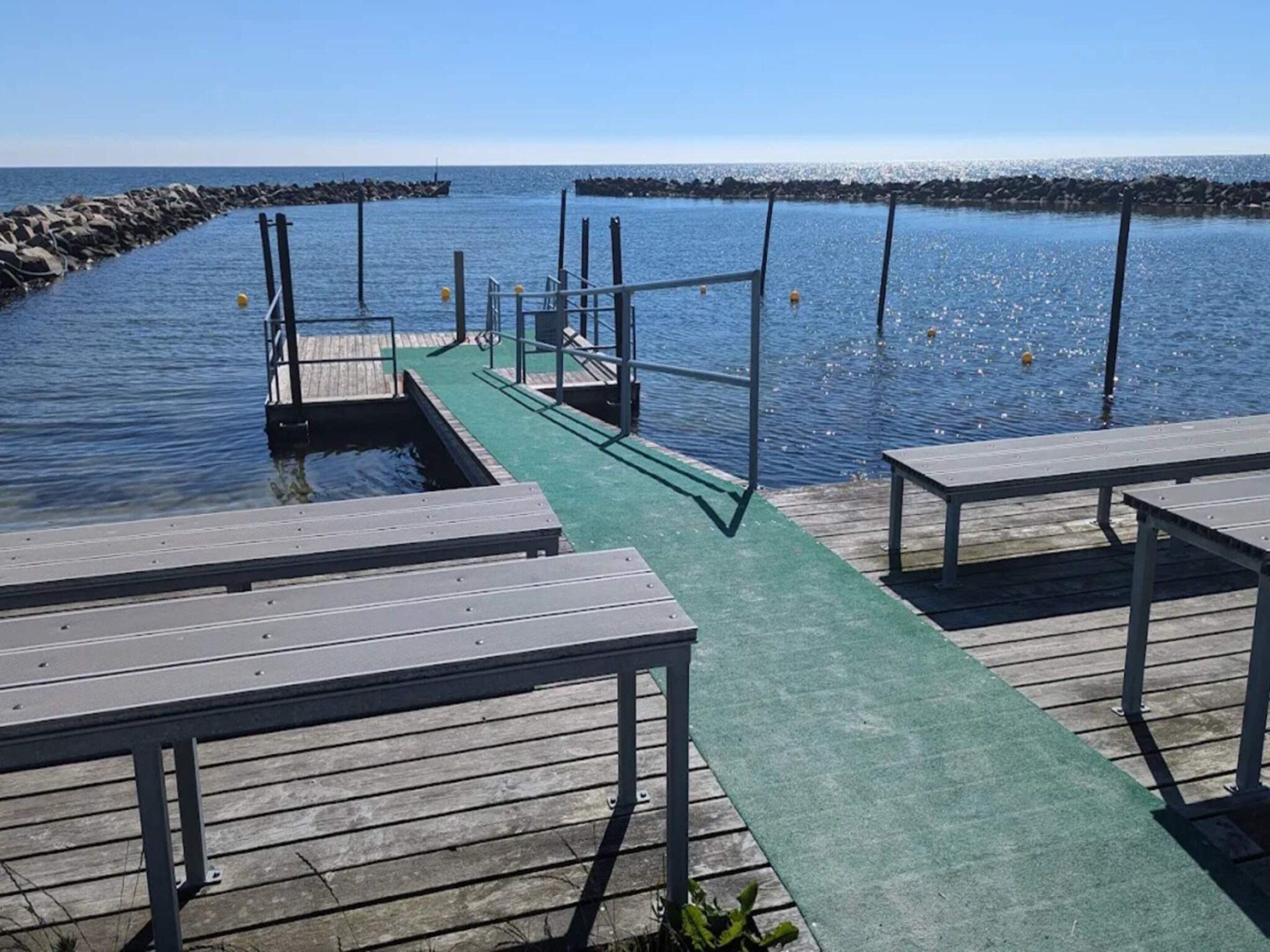 A wooden pier extending into calm water with a green walkway, benches, and a metal railing.