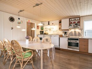 A modern kitchen with white cabinets, a stainless steel range hood, and a dining area with wicker chairs and a round table.