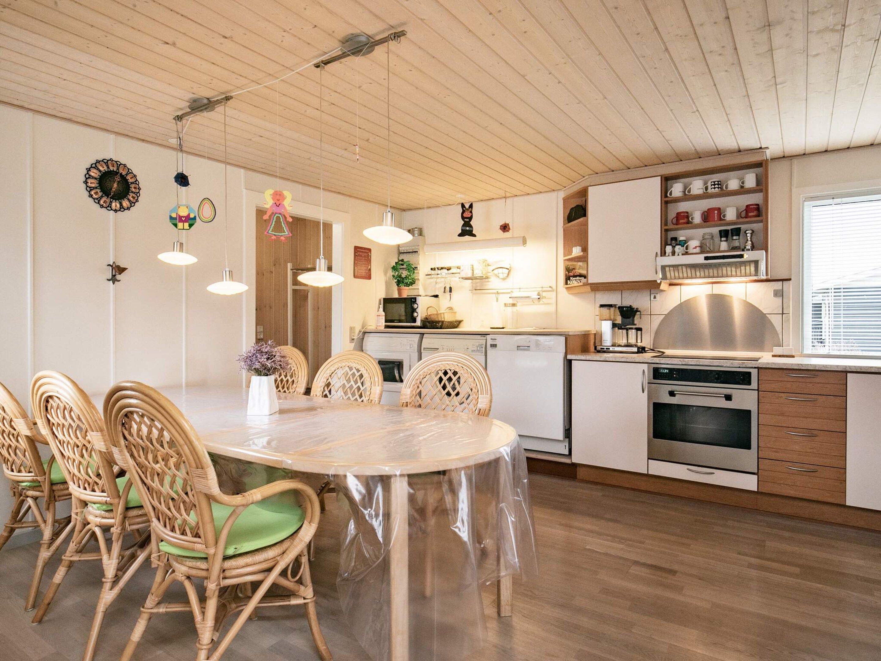 A modern kitchen with white cabinets, stainless steel appliances, and a dining area with wicker chairs and a round table.