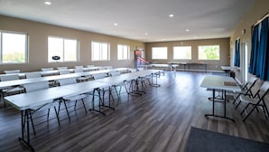 A spacious room with multiple tables and chairs, large windows, and a basketball hoop.