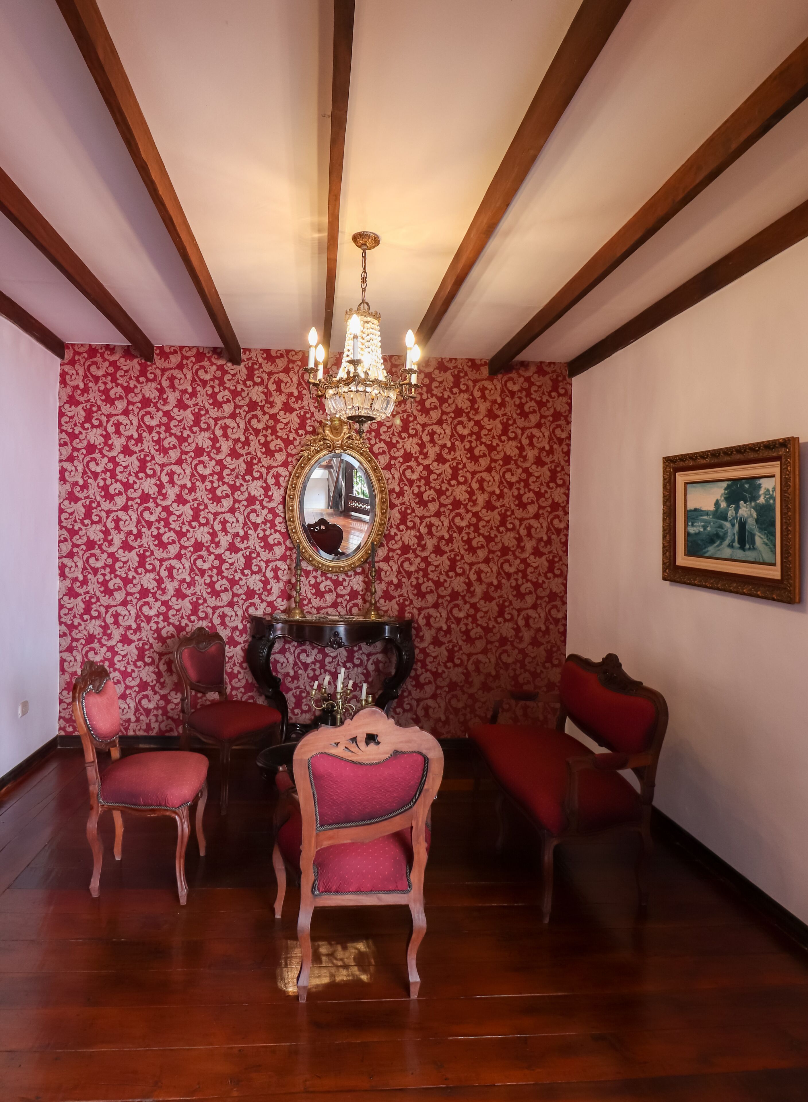 Una habitación con techo de madera, un candelabro, un espejo y cuatro sillas con cojines rojos.
