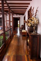 Un pasillo de madera con un banco, un jarrón grande con flores y un mueble de madera.