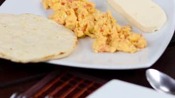 A white plate with scrambled eggs, a slice of bread, and a glass of water on a wooden table.