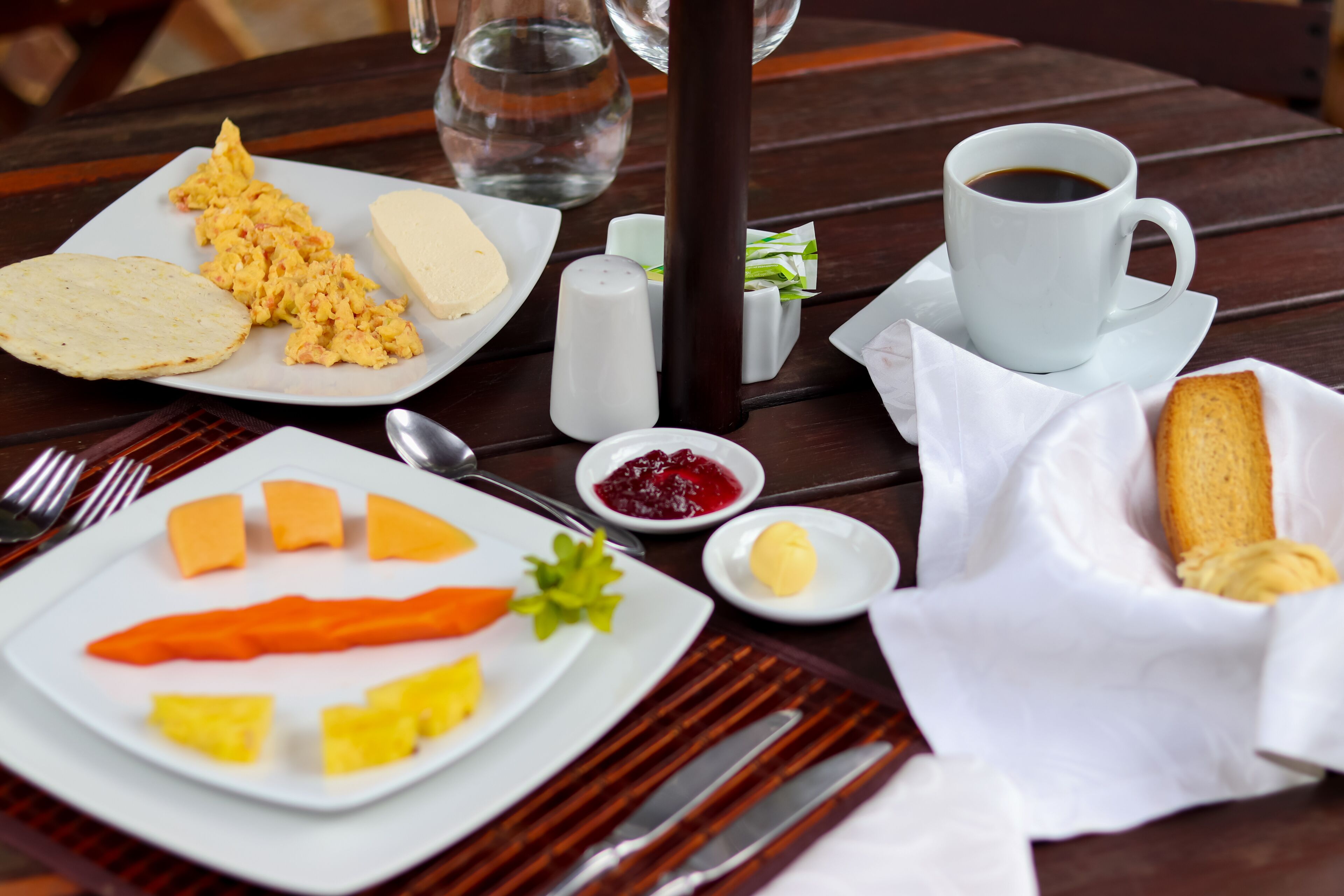 A breakfast table with scrambled eggs, toast, butter, jam, and a cup of coffee.