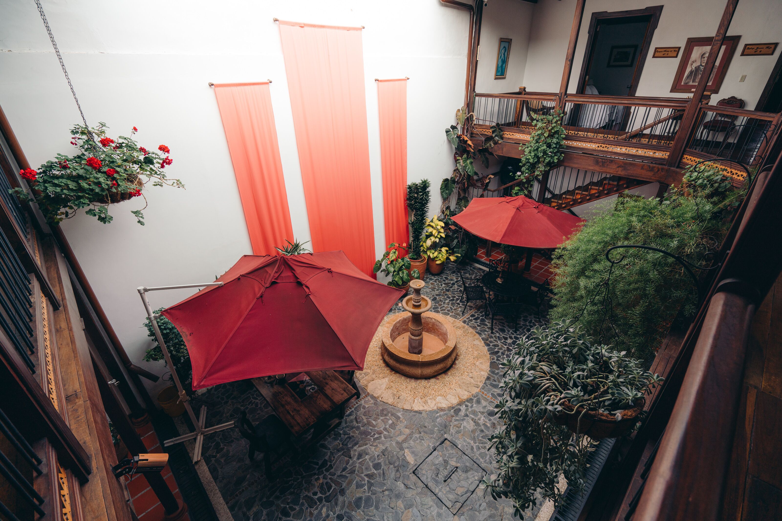 A courtyard with a fountain, potted plants, and red umbrellas.
