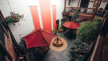 A courtyard with a fountain, potted plants, and red umbrellas.