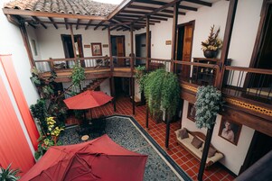 Un patio con un paraguas rojo, plantas en macetas y un banco de madera.