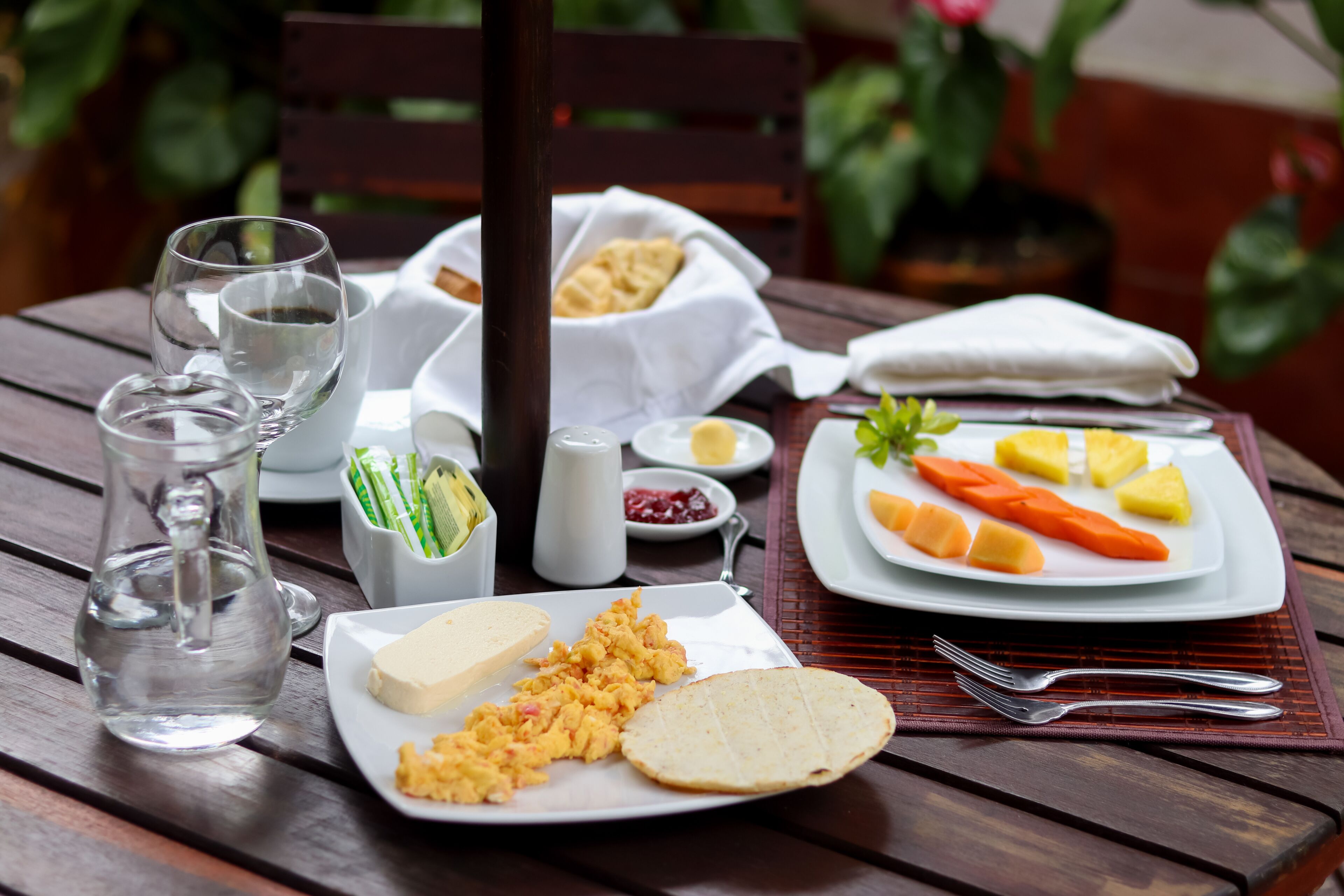 Una mesa servida con alimentos para el desayuno, como huevos revueltos, tostadas, fruta y bebidas.