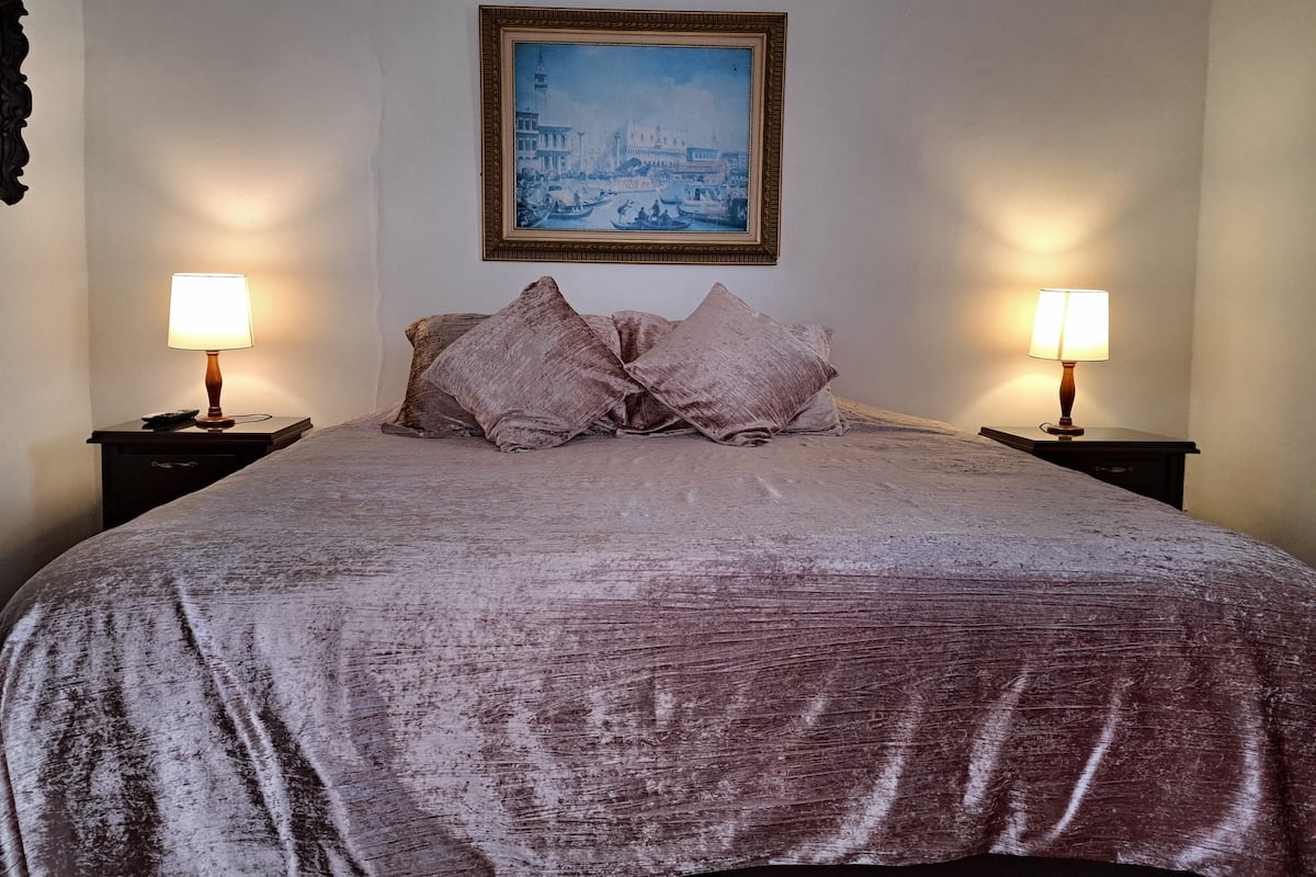 Een bed met een geruite sprei, twee nachtkastjes met lampen, en een gekaderd schilderij aan de muur.