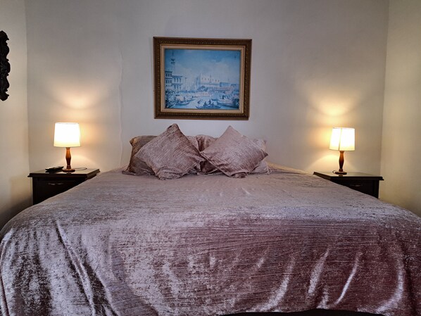 A bed with a textured bedspread, two nightstands with lamps, and a framed painting on the wall.