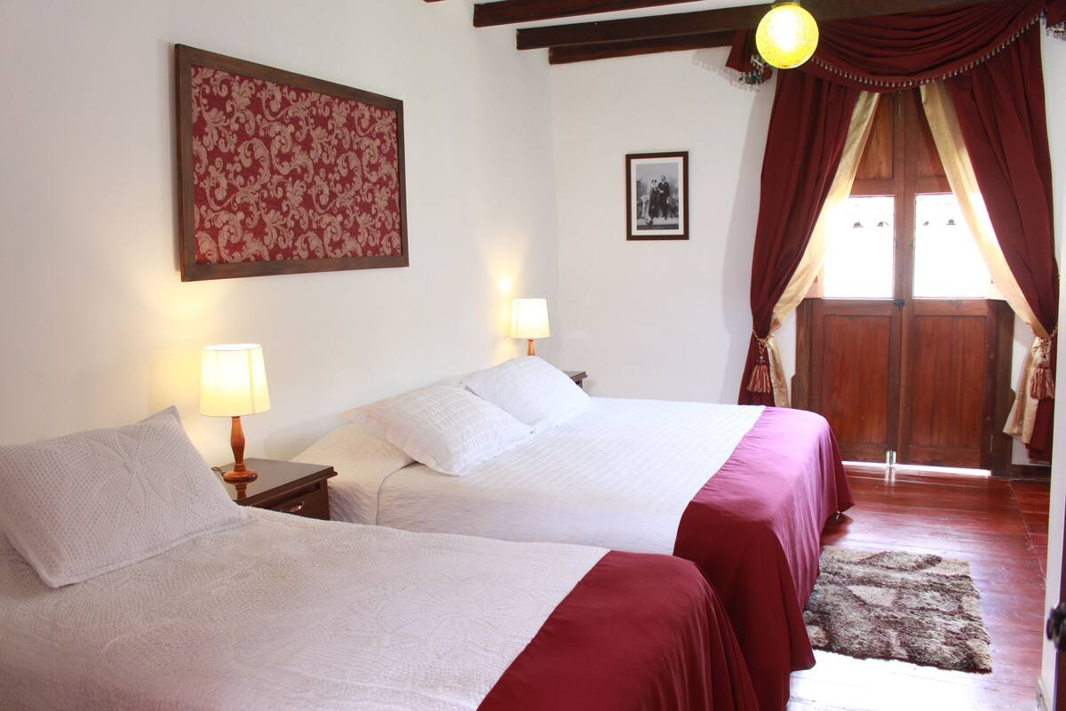 Een slaapkamer met twee bedden, een houten deur en een rood gordijn.
