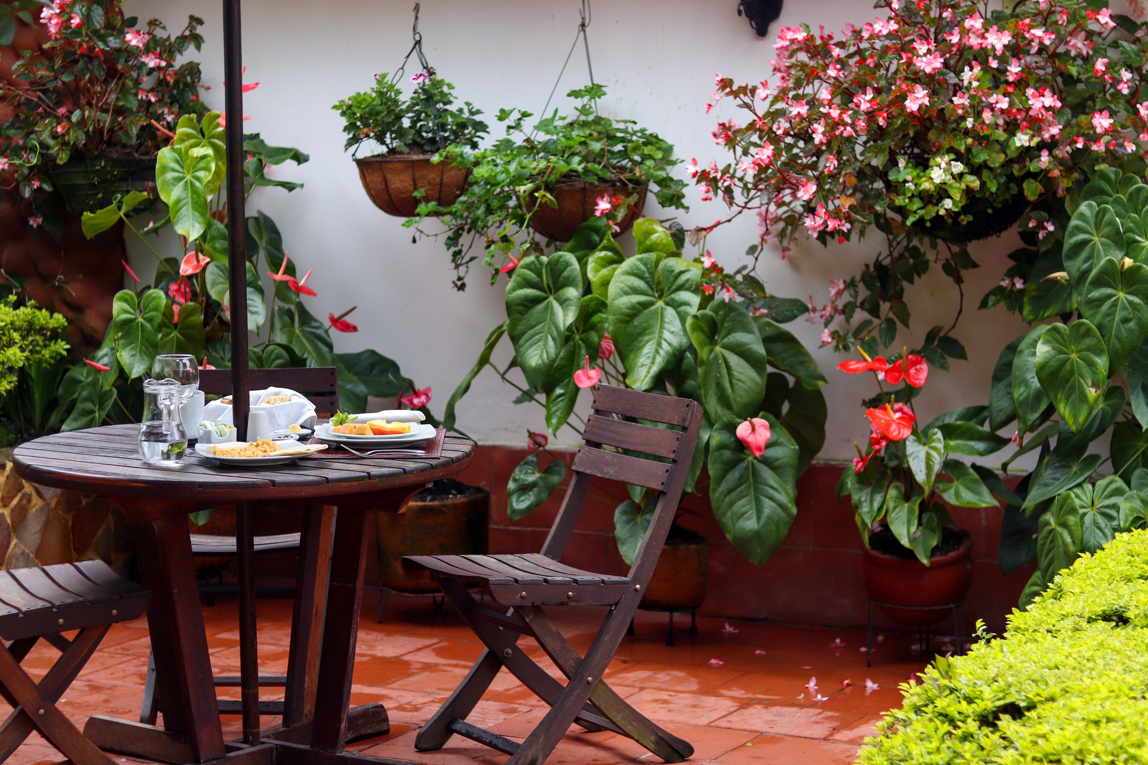 Un patio con una mesa redonda de madera, dos sillas de madera, una silla colgante y varias plantas en macetas.