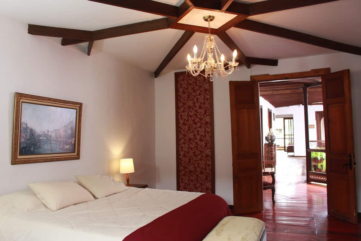 Een slaapkamer met een groot bed, een kroonluchter, een schilderij en een uitzicht door een open deur.