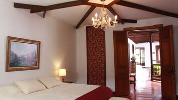 A bedroom with a large bed, a chandelier, a painting, and a view through an open door.