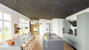 Une cuisine moderne dotée d’un îlot central, de grandes fenêtres et d’un coin repas avec des chaises en bois.