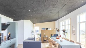 Une cuisine moderne dotée d’un îlot central, d’un coin repas avec une longue table et de grandes fenêtres qui laissent entrer la lumière naturelle.