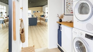 Une cuisine moderne dotée d’un lave-linge et d’un sèche-linge intégrés, d’un plancher en bois et d’un coin repas visible à travers une porte ouverte.