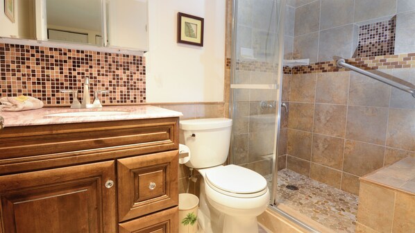 A bathroom with a wooden vanity, a toilet, a shower with a glass door, and a tiled backsplash.