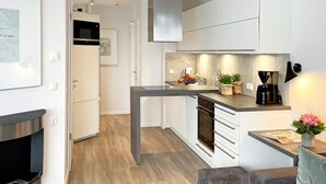 A modern kitchen with white cabinetry, a built-in oven, and a dining area with a grey sofa and a small table.