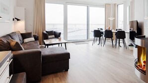 A modern living room with a sofa, a dining area with chairs, a flat-screen TV, and a fireplace.