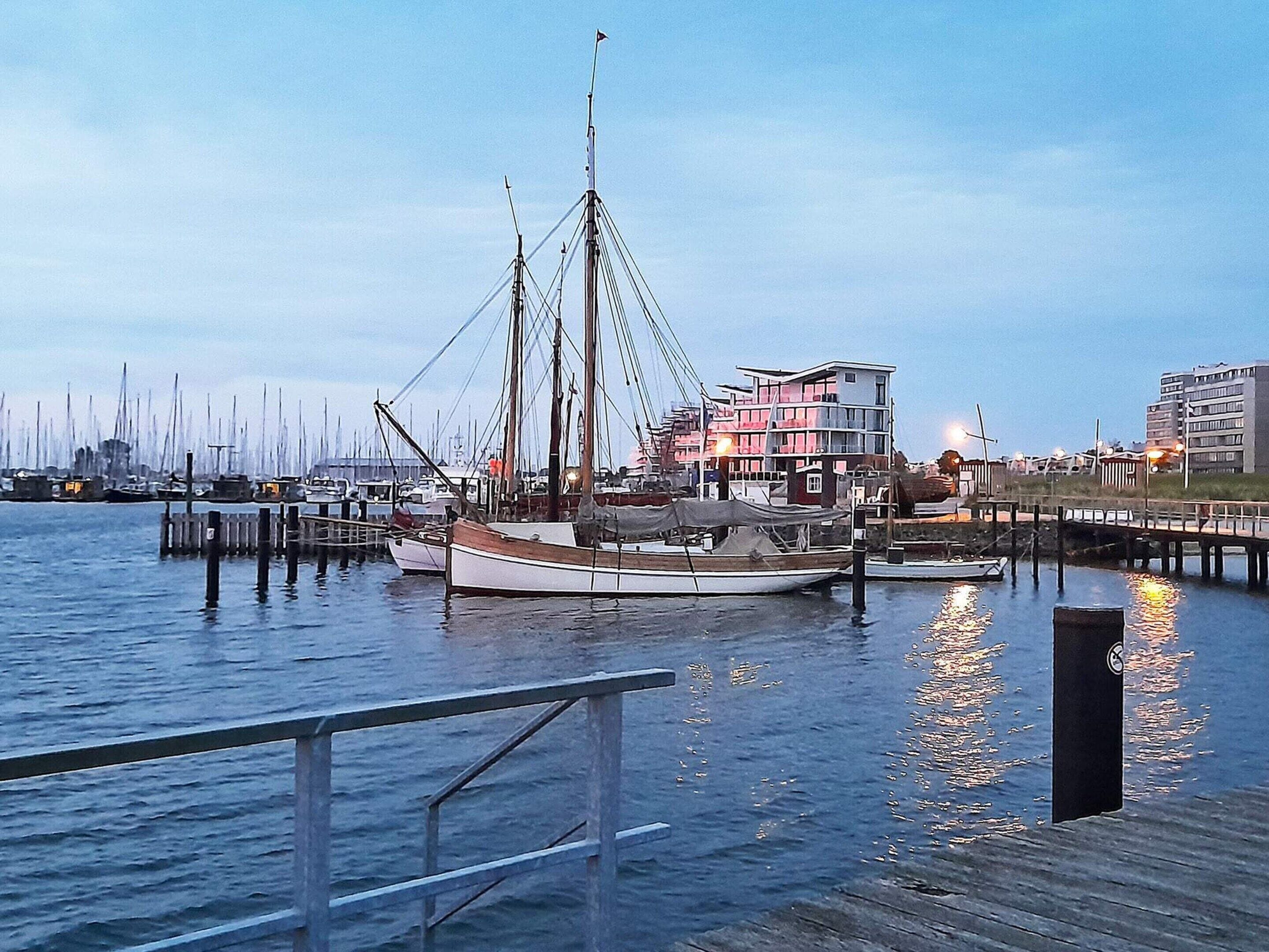A marina with boats docked, a wooden pier, and buildings in the background.
