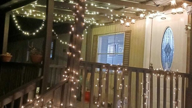 A house with a porch decorated with string lights, a wooden railing, and a window with shutters.