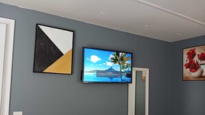 A room with a grey wall, a flat-screen TV mounted above a white-framed mirror, and two framed artworks.