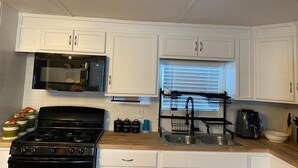 A kitchen with white cabinets, a black stove, a microwave, and a window with blinds.