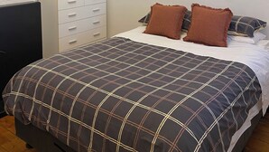 A bedroom with a bed, a dresser, an air conditioner, and two wall-mounted pictures.