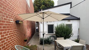 A patio with a table and chairs, a hanging chair, a large umbrella, and a potted plant.