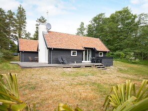 Une cabane à deux étages, avec un toit en tuiles, une antenne parabolique et une terrasse dotée de meubles d’extérieur.