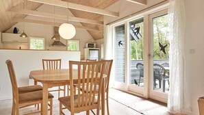 A dining area with a wooden table and chairs, a kitchen with a microwave, and a sliding glass door leading to an outdoor deck. - 6 Person Holiday Home in Aakirkeby (Akirkeby)