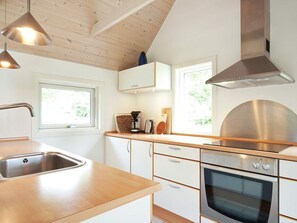 Une cuisine moderne dotée d’un évier en acier inoxydable, d’un plan de travail en bois, d’un four encastré et de luminaires suspendus.