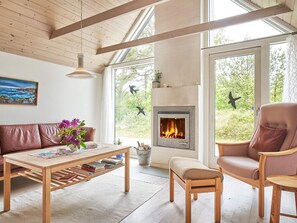 A cozy living room with a fireplace, wooden furniture, and large windows.