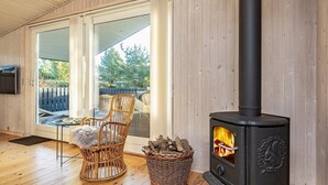 Une pièce chaleureuse avec un plancher en bois, un fauteuil en osier, un panier en osier et un poêle à bois noir.
