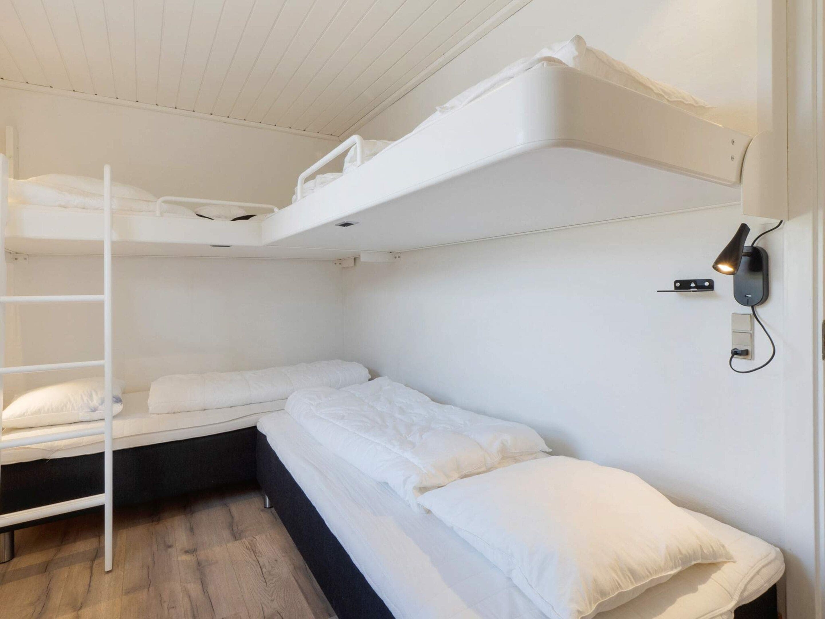 Une chambre avec un lit superposé, une échelle, une lampe fixée au mur et une prise de courant.