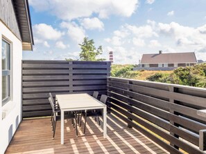 A wooden deck with a table and chairs, a fence, and a building in the background. - 5 Star Holiday Home in Thisted (Thisted)