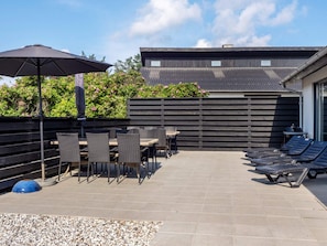An outdoor patio area with a table and chairs, a lounge area with sun loungers, and a building with a corrugated metal roof. - 5 Star Holiday Home in Thisted (Thisted)