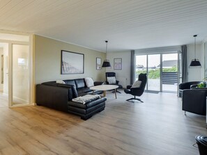 A modern living room with a black leather sofa, a round coffee table, and a black armchair. There are two pendant lights, a framed picture on the wall, and a sliding glass door leading to an outdoor area. - 5 Star Holiday Home in Thisted (Thisted)