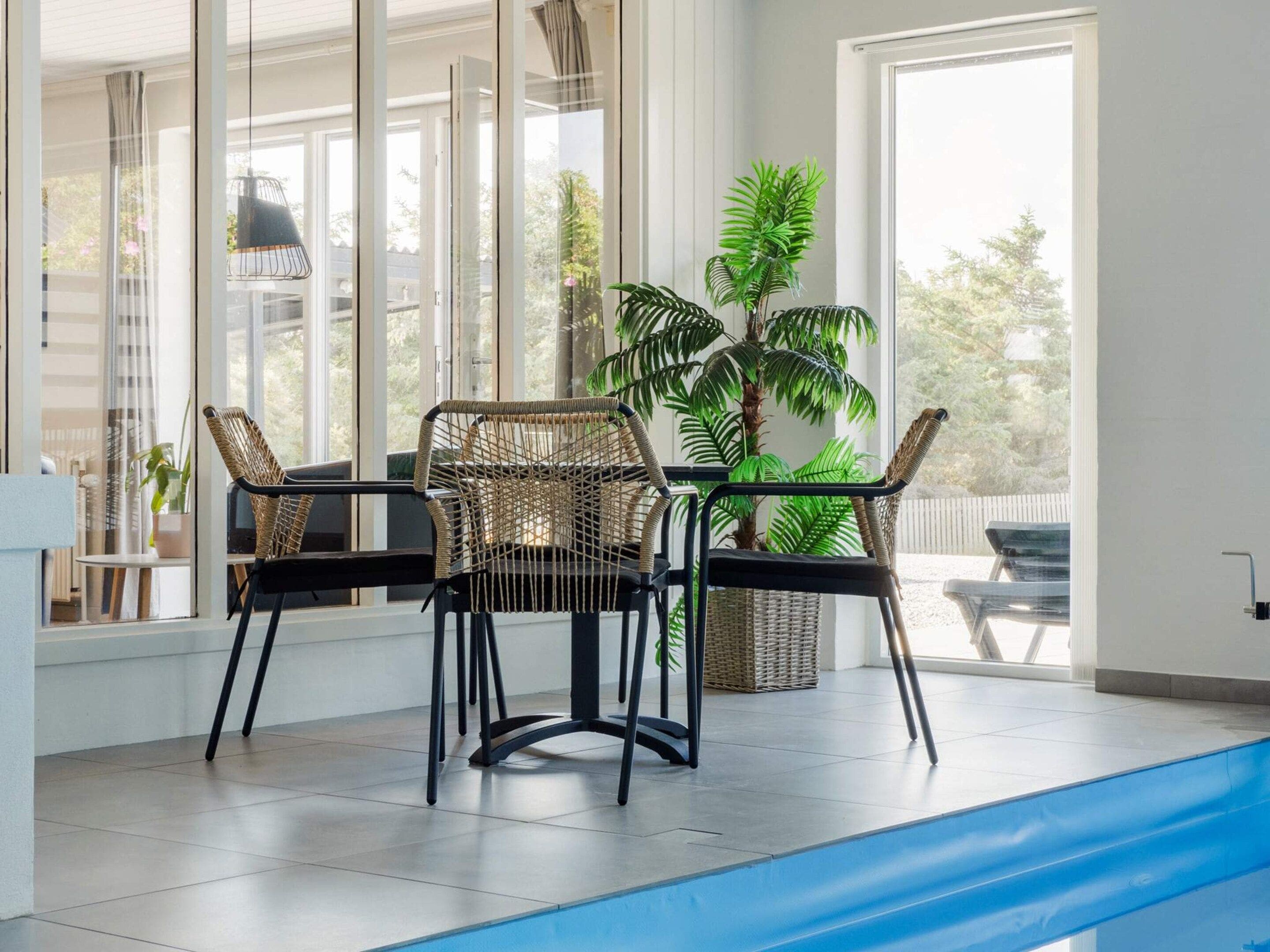 A room with a large window, a pool, and two wicker chairs.