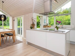 A modern kitchen with a large island, wooden dining table, and chairs, with a view of greenery outside. - 6 Person Holiday Home in Oksbol (Oksbol)