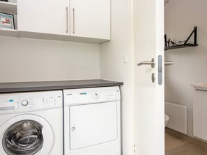 A compact laundry area with a front-loading washing machine, a small shelf with a no-smoking sign, and a black metal shelf with decorative items. - 6 Person Holiday Home in Oksbol (Oksbol)