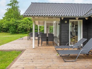 A covered outdoor area with a wooden deck, a table with chairs, and two lounge chairs.