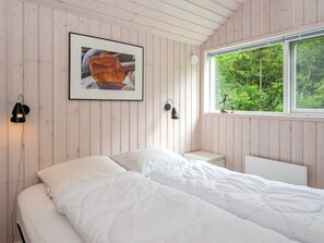 A bedroom with a bed, a framed picture on the wall, a window with a view of trees, and two wall-mounted lamps.