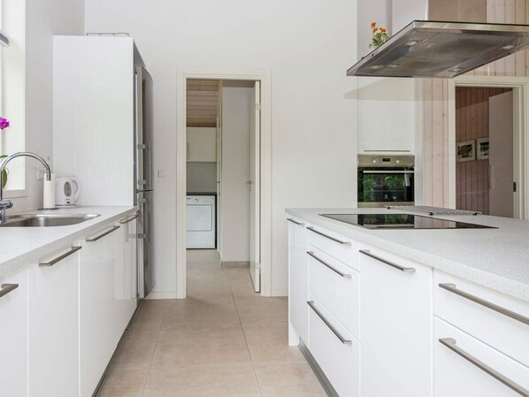 A modern kitchen with white cabinetry, a stainless steel range hood, and a built-in oven.