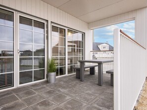 A covered patio area with a table and benches, large sliding glass doors, and a potted plant.