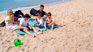A group of people sitting on a beach with a soccer ball and a blue towel. - 4 Star Holiday Home in Ringkobing (Ringkobing)