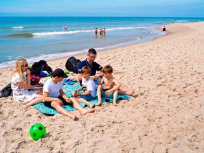 En grupp människor sitter på en strand med en fotboll och ett blått handduk.