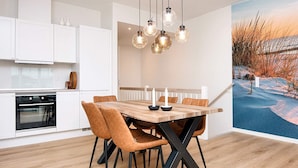 Una cocina moderna con armarios blancos, una mesa de comedor de madera con sillas, y luces colgantes.